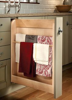 an open cabinet in the middle of a kitchen with towels hanging from it's sides