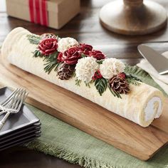 a roll decorated with flowers and pine cones on a cutting board next to silverware