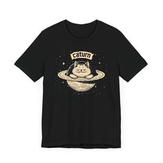 Caturn T-Shirt - Cosmic Cat Planet Graphic Tee 🌌🐱 Welcome to Caturn, the cutest planet in the galaxy! Our Caturn T-Shirt features an adorable cat lounging on Saturn’s rings, perfect for space enthusiasts and cat lovers alike. Made from high-quality fabric, this tee ensures both comfort and durability for your everyday adventures. Add a touch of cosmic cuteness to your wardrobe with this whimsical and unique graphic tee! 🌟✨ Why You'll Love It: 👕 Ultimate Comfort: Made with 100% Airlume combed Cat Lounging, Planet Graphic, Cosmic Cat, Cat Lounge, Everyday Adventures, The Galaxy, Leisure Wear, Black Tee, The Cutest