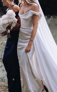 two women in wedding gowns are walking side by side with one holding a bouquet