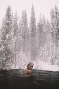 a woman sitting in a hot tub surrounded by snow covered trees