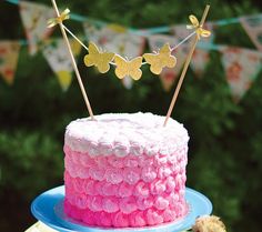 a cake with pink frosting and gold butterflies on top is sitting on a blue plate