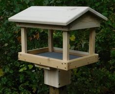 a wooden bird feeder in front of some bushes