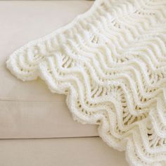 a white crocheted blanket sitting on top of a couch next to a pillow