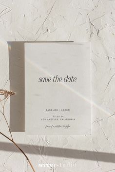 a white save the date card sitting on top of a table next to dried flowers