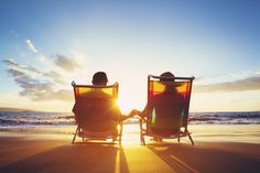 two people sitting in beach chairs facing each other on the beach, with the sun shining behind them