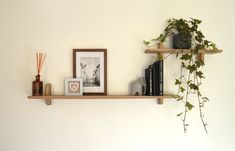 two wooden shelves with books and plants on them next to a wall mounted photo frame