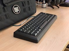 a black computer keyboard sitting on top of a wooden desk next to a laptop bag