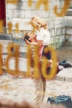 a man and woman kissing in front of a building with the word love spelled on it