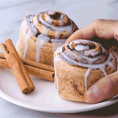 two cinnamon rolls on a white plate with cinnamon sticks