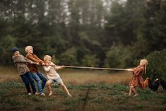 an older man pulling two young children on a rope in a field with chickens behind him