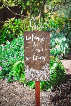 a wooden sign that says welcome to our wedding on it in front of some plants