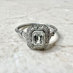 an antique style diamond engagement ring on a white surface with the center stone surrounded by smaller diamonds