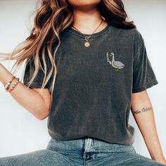 "🦢💕 Add a playful twist to your daily look with our \"Silly Goose\" Embroidered T-Shirt! This charming shirt brings a splash of whimsy to your outfit, featuring a uniquely embroidered goose that's not just silly but ready to take on the world. Crafted with attention to detail, this Embroidered Shirt showcases a goose in a stance that's both playful and assertively fun. Made from high-quality materials, our T-Shirt offers both comfort and durability, ensuring you can enjoy wearing it time and time again. Whether you're drawn to Simple Embroidery or in search of a piece that showcases your love for fun and humor with a Funny Goose Shirt, this \"Silly Goose\" T-Shirt is the perfect pick. Don't just wear any shirt; choose one that reflects your quirky personality and love for all things ligh Casual Everyday Tops With Embroidered Text, Casual Tops With Embroidered Text For Everyday, Trendy Embroidered Relaxed Fit Tops, Everyday Crew Neck Tops With Embroidered Graphics, Crew Neck Top With Embroidered Graphics For Everyday, Short Sleeve Tops With Graphic Embroidery For Everyday, Short Sleeve Tops With Embroidered Graphics For Everyday, Casual Embroidered Everyday T-shirt, Casual Everyday Embroidered T-shirt