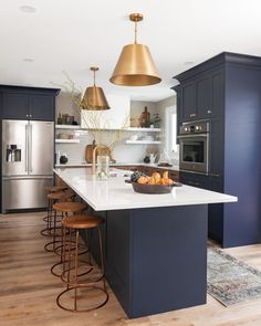 a large kitchen with blue cabinets and white counter tops, gold pendant lights over the island