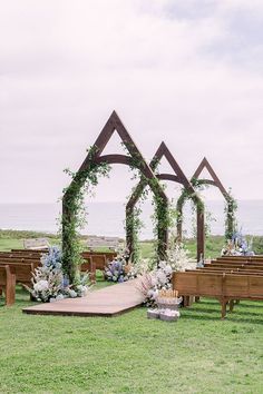 an outdoor ceremony setup with wooden benches and flowers on the grass, along with greenery