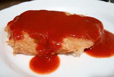 a piece of meatloaf on a white plate covered in ketchup and sauce