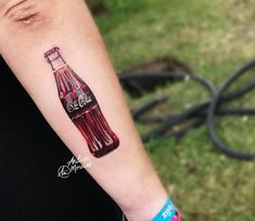 a person with a tattoo on their arm that has a coca cola bottle painted on it