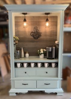 a blue cabinet with coffee cups on top and lights hanging from it's sides