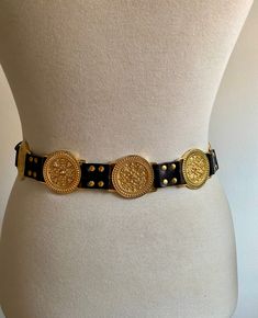 Vintage imitation leather belt with studs and medallions worked in gold-colored metal from the early 1990s. Reminiscent of the typical Versace belt of those years. It is a belt that has its own "weight", exactly 330 grams, given by the fact that it has 10 gold-colored medallions worked on the external side, one of which has the function of closing the belt. It's a belt that catches the eye. Worn very little, it is still in excellent condition. It only has a few micro marks on the edge of some of Vintage Belts Women, Vintage Leather Belt With Gold Buckle, Luxury Vintage Belts With Brass Hardware, Luxury Gold-tone Belt Buckle For Formal Wear, Luxury Gold Belt With Antique Buckle, Luxury Gold Belt With Brass Buckle, Versace Belt, Gold Belts