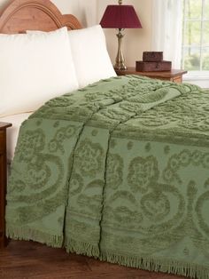 a green bedspread with white pillows and a lamp on the nightstand next to it