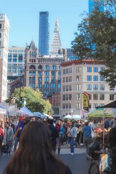 a crowd of people walking down a street next to tall buildings in the background,