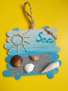 a wooden sign that says sea with shells on the sand and rope hanging from it