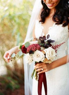 a bride holding a bouquet of flowers in her left hand and smiling at the camera