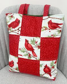 a red and white tote bag sitting on top of a gray couch next to a grey chair