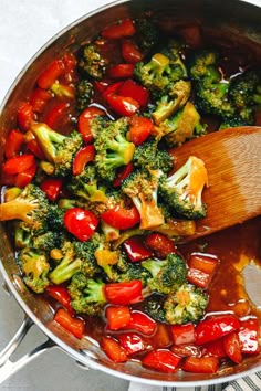 broccoli, tomatoes and other vegetables are being cooked in a pan with a wooden spoon