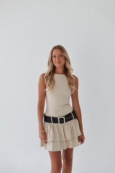 a woman posing for the camera wearing a tan dress and black belted sandals with her hands in her pockets