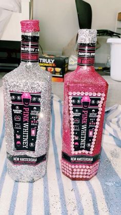 two bottles are sitting on a table with silver and pink glitter covering them, one is empty