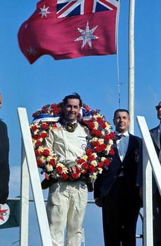 the man is holding a wreath with two other men in suits standing behind him and looking at the camera