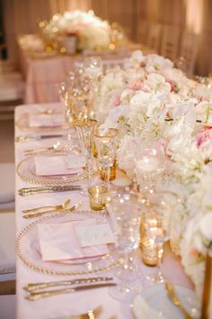 the table is set with white flowers and gold place settings for an elegant wedding reception