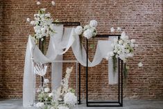 an arrangement of white flowers and ribbons on display in front of a brick wall,