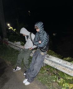 two young boys standing next to each other on a sidewalk at night with the lights on