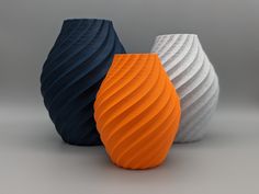 three different colored vases sitting next to each other on a gray surface with grey background