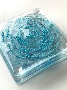 a glass dish with beads on it sitting on a counter top in front of a white background