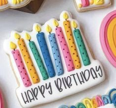 decorated birthday cookies with candles and rainbow decorations on a white tablecloth next to other cookie items