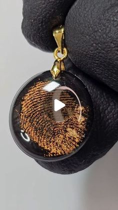 a hand holding a black and gold pendant with an image of a fingerprint on it