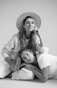 two women sitting on the floor with one holding her head to her ear and the other leaning over her shoulder