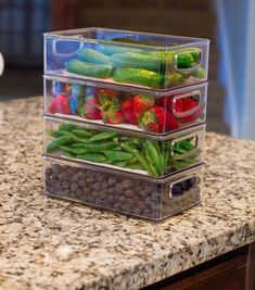 three plastic containers filled with fruits and vegetables on top of a granite countertop in a kitchen