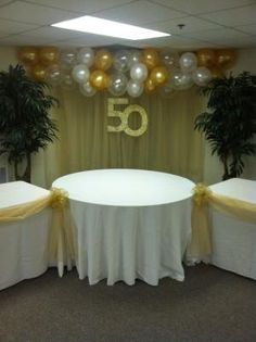 the table is set up with white linens and gold ribbon for 50th birthday decorations