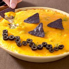 a bowl filled with food topped with black chips and an orange face made out of tortilla chips