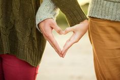 two people holding hands making a heart shape with their hands while standing next to each other