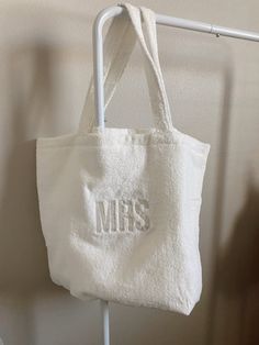 a white tote bag hanging on a clothes rack with the word mrs printed on it