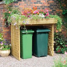 two green trash cans sitting next to each other in front of a building with flowers growing on the roof