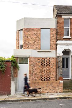 a woman walking her dog past a brick house