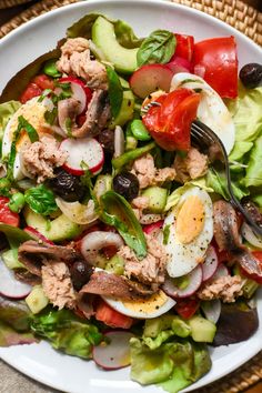 a white plate topped with salad and an egg on top of lettuce next to tomatoes