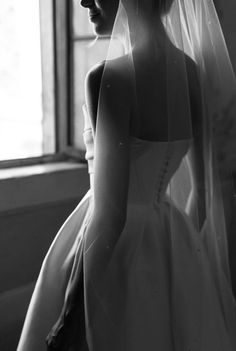 a woman in a wedding dress looking out the window